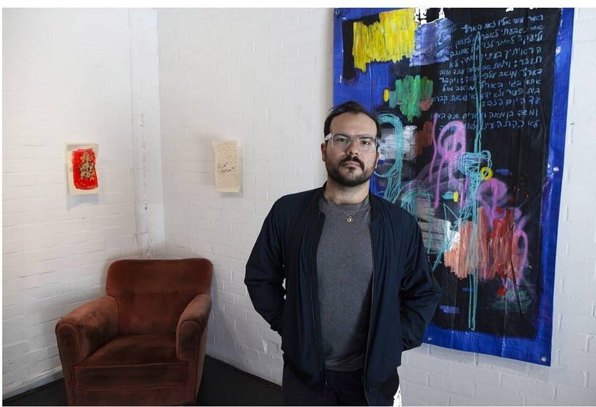 Gregory Uzelac standing beside a blue painted canvas