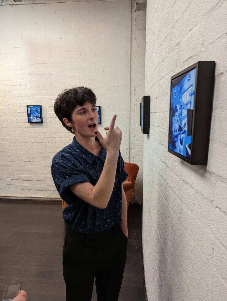 Nicole Welsh talking beside framed blue paintings
